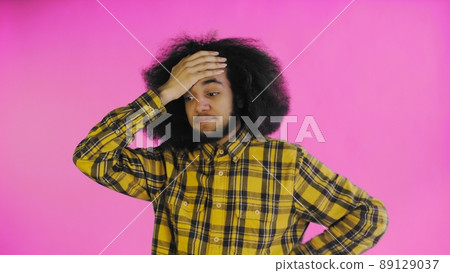 A young man with an African hairstyle on a pink background is surprised. Emotions on a colored background. A young man with an African hairstyle on a pink background is surprised. Emotions on a colored background. 89129037