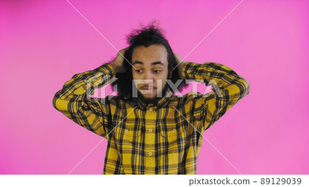 A young man with an African hairstyle on a pink background is surprised. Emotions on a colored background. A young man with an African hairstyle on a pink background is surprised. Emotions on a colored background. 89129039