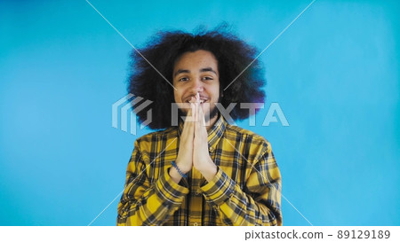 A young man with an African hairstyle on a blue background is happy. Emotions on a colored background. 89129189