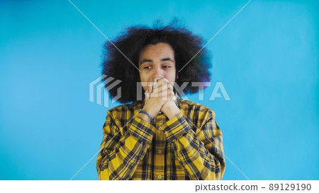 A young man with an African hairstyle on a blue background is happy. Emotions on a colored background. A young man with an African hairstyle on a blue background is happy. Emotions on a colored background. 89129190