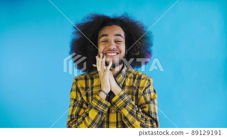 A young man with an African hairstyle on a blue background is happy. Emotions on a colored background. A young man with an African hairstyle on a blue background is happy. Emotions on a colored background. 89129191
