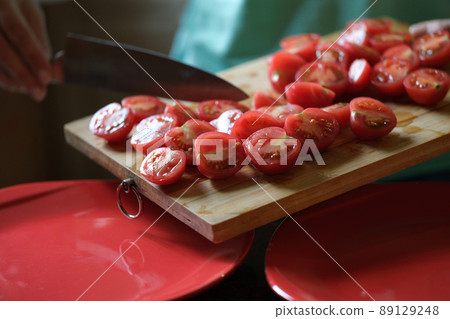 Cook putting sliced tomatoes on red plate closeup 89129248