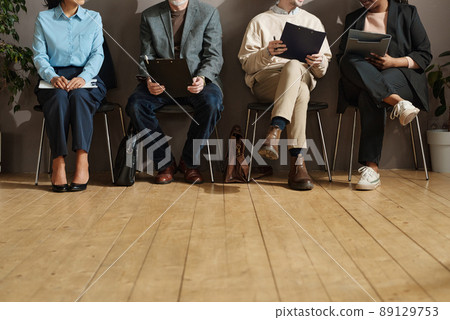 Close-up of people sitting on chairs and filling forms at office corridor 89129753