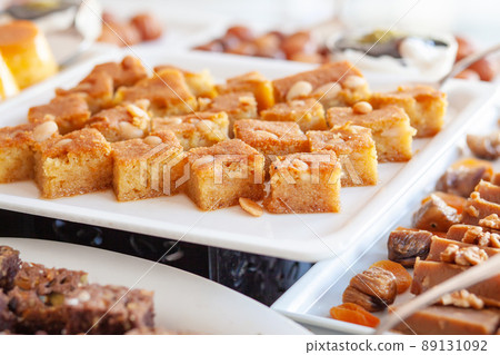 Semolina cake, or Revenue, Revani or Ravani. Made from a combination of semolina and flour and soaked in a citrus infused syrup. Various cakes and sweets on buffet 89131092
