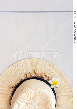 Summer beach straw hat with a necklace with shells and pearls and the plumeria flower on the tiled floor, top view. 89131110