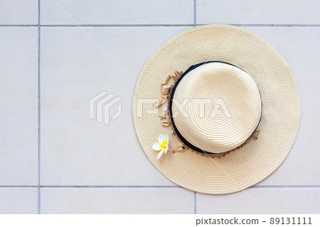 Summer beach straw hat with a necklace with shells and pearls and the plumeria flower on the tiled floor, top view. 89131111
