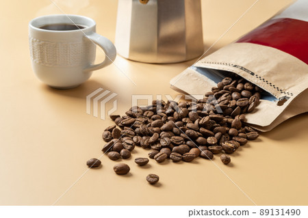 Organic coffee beans spilled out of a brown paper bag on a beige background. Organic coffee beans spilled out of a brown paper bag on a beige background. 89131490