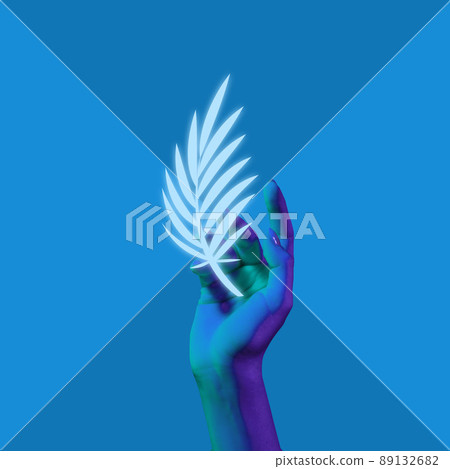 Contemporary art collage. Painted hand holding white leaf or plumelet isolated on blue background. Monochrome. Beauty, art, creativity concept Contemporary art collage. Painted hand holding white leaf or plumelet isolated on blue background. Monochrome. Beauty, art, creativity concept 89132682