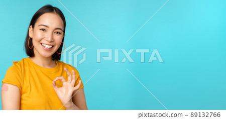 Vaccine campaign from covid-19. Happy healthy asian girl showing okay sign and smiling, bandaid on shoulder from coronavirus vaccination, blue background Vaccine campaign from covid-19. Happy healthy asian girl showing okay sign and smiling, bandaid on shoulder from coronavirus vaccination, blue background 89132766
