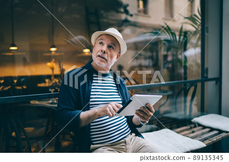 Pondering Caucasian senior with digital tablet thinking about network blogging 89135345