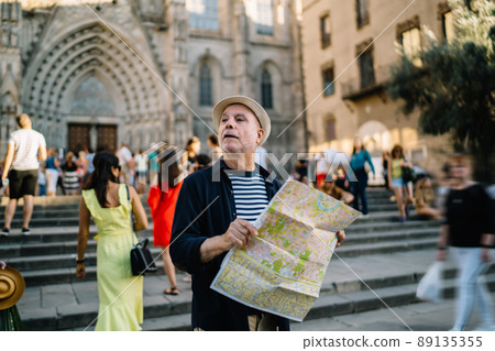 Caucasian man in straw hat holding location map at square in town 89135355