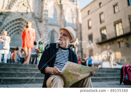 Caucasian man in straw hat holding location map resting at square in town 89135388