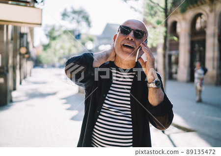 Stylish male tourist in sunglasses connecting to roaming internet for calling to friend on vacations, Stylish male tourist in sunglasses connecting to roaming internet for calling to friend on vacations, 89135472