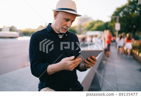 Elderly tourist using digital tablet for browsing publication and make booking 89135477