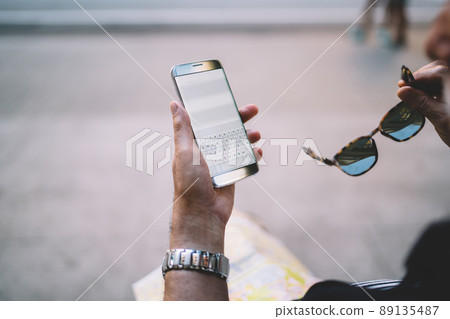 Unrecognizable man reading text publication during text chatting on cellphone Unrecognizable man reading text publication during text chatting on cellphone 89135487