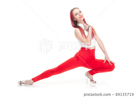 A beautiful, athletic, slender, smiling and cheerful woman in a white top and red sweatpants performs elements of the strip plastic dance. Lifestyle concept with sports and gym, healthy lifestyle 89135719