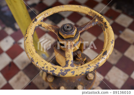 Close-up at pipeline valve which is using to control production process in the oil refinery plant. Selective focus at the valve handle wheel, Heavy industrial object photo. 89136010