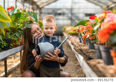 Mom and her son with a watering can in the greenhouse Mom and her son with a watering can in the greenhouse 89136278