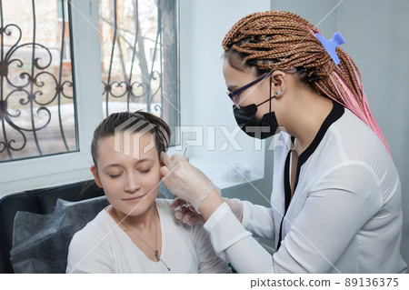 piercings on an ear. Conch and helix piercings close up. Professional holding the jewel. 89136375