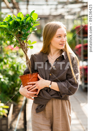 Portrait of a woman worker of garden center with a potted plant in her hands Portrait of a woman worker of garden center with a potted plant in her hands 89136425