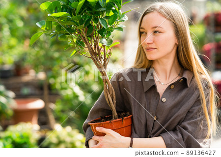 Girl florist with a plant in a pot in her hand looks to the side 89136427