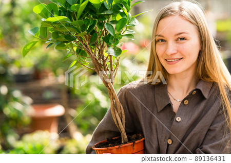 Close-up portrait of pretty greenhouse worker with plant 89136431