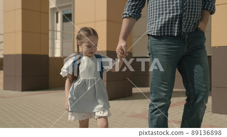 father holds happy daughter by the hand, accompany little child with backpack to school, study in preschool preparation, walk through schoolyard, first grade student with school bag on his shoulders 89136898