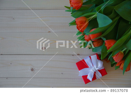Pink tulips with green leaves lie in the upper corner on a wooden background, and next to it is a gift in a red package with a bow. High quality photo Pink tulips with green leaves lie in the upper corner on a wooden background, and next to it is a gift in a red package with a bow. High quality photo 89137078