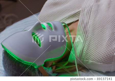 LED light anti-aging mask for facial skin care in a spa slow motion. A woman lies on a couch in a special mask. Modern technologies of beauty and health. LED light anti-aging mask for facial skin care in a spa slow motion. A woman lies on a couch in a special mask. Modern technologies of beauty and health. 89137141
