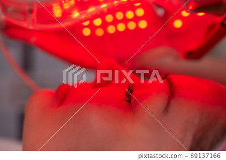 LED light anti-aging mask for facial skin care in a spa slow motion. A woman lies on a couch in a special mask. Modern technologies of beauty and health. 89137166