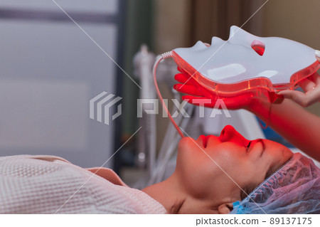 LED light anti-aging mask for facial skin care in a spa slow motion. A woman lies on a couch in a special mask. Modern technologies of beauty and health. LED light anti-aging mask for facial skin care in a spa slow motion. A woman lies on a couch in a special mask. Modern technologies of beauty and health. 89137175