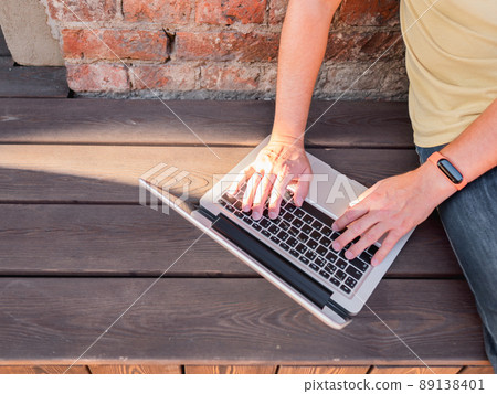 Top view on man's hands on computer keyboard. Freelancer works outdoors with laptop. Modern lifestyle. Open air workplace. Top view on man's hands on computer keyboard. Freelancer works outdoors with laptop. Modern lifestyle. Open air workplace. 89138401