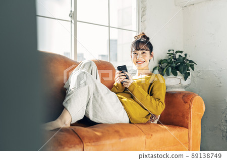 A woman holding a smartphone on the sofa 89138749