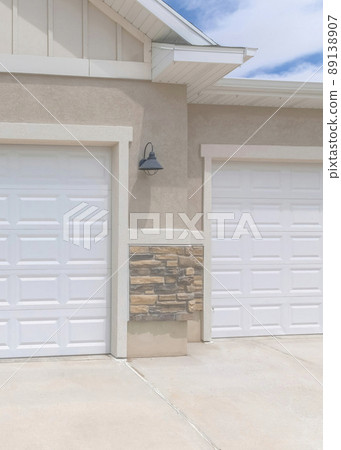 Vertical Whispy white clouds Exterior of a garage with white double sectional doors and wall mounted lighting fixtures Vertical Whispy white clouds Exterior of a garage with white double sectional doors and wall mounted lighting fixtures 89138907