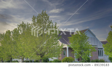 Panorama Whispy white clouds Corner house with bricks siding, flowers and trees on the lawn a Panorama Whispy white clouds Corner house with bricks siding, flowers and trees on the lawn a 89139183