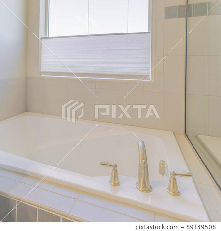 Square Drop in bathtub in a corner against the window with blinds 89139508