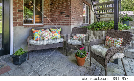 Panorama Woven couch and armchairs on an outdoor patio under the deck of a house with bricks Panorama Woven couch and armchairs on an outdoor patio under the deck of a house with bricks 89139583