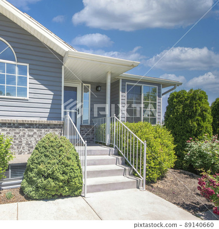 Square White puffy clouds Facade of a house with shrubs, trees and lawn at the front 89140660