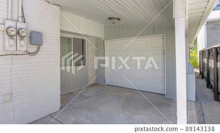 Panorama Small garage at the side of a house with white siding and two electricity meters Panorama Small garage at the side of a house with white siding and two electricity meters 89143138
