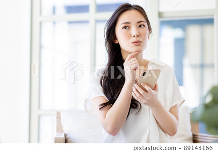 A woman thinking with a smartphone in one hand A woman thinking with a smartphone in one hand 89143166
