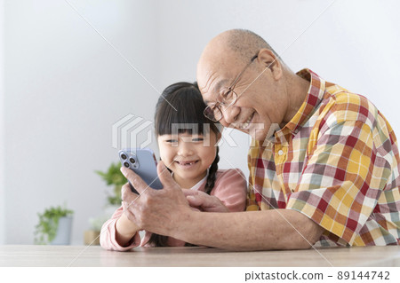 Grandfather and granddaughter looking at smartphone together Grandfather and granddaughter looking at smartphone together 89144742