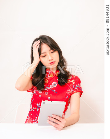Young asian woman wearing traditional cheongsam feeling tired and bad spirit while using tablet computer and having headache touching head discomfort in front of white background Young asian woman wearing traditional cheongsam feeling tired and bad spirit while using tablet computer and having headache touching head discomfort in front of white background 89144931
