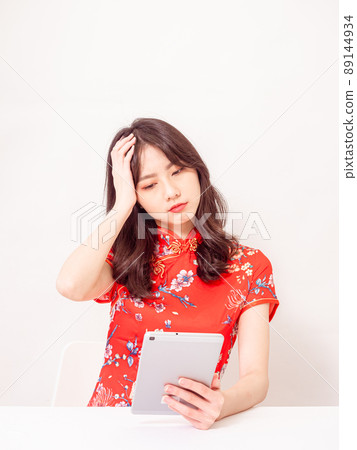 Young asian woman wearing traditional cheongsam feeling tired and bad spirit while using tablet computer and having headache touching head discomfort in front of white background Young asian woman wearing traditional cheongsam feeling tired and bad spirit while using tablet computer and having headache touching head discomfort in front of white background 89144934