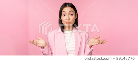 Portrait of confused asian businesswoman shrugging shoulders, looking clueless and puzzled, dont know, cant say, standing over pink background in office suit Portrait of confused asian businesswoman shrugging shoulders, looking clueless and puzzled, dont know, cant say, standing over pink background in office suit 89145776