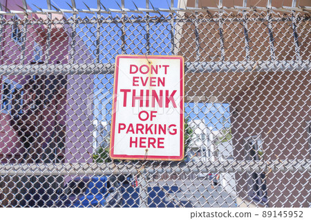Don't even think of parking here signage on a metal mesh fence in San Francisco, California 89145952