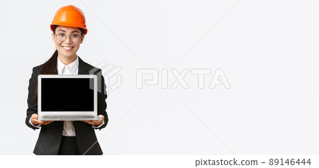 Smiling professional female asian engineer introduce construction plan to investors or clients, standing in safety helmet and suit showing laptop screen with pleased smile, white background Smiling professional female asian engineer introduce construction plan to investors or clients, standing in safety helmet and suit showing laptop screen with pleased smile, white background 89146444