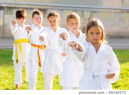 Tween girls and boys exercising taekwondo techniques on green lawn 89146575