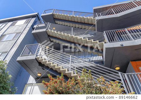 Low angle view of an apartment building with three outdoor straight staircase with metal railings Low angle view of an apartment building with three outdoor straight staircase with metal railings 89146662