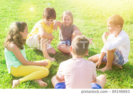 Children friends sitting on grass together and chatting 89146663