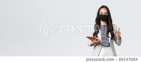 Business, finance and employment, covid-19 preventing virus and social distancing concept. Smiling real estate broker wearing protective mask during meeting, pointing camera, hold digital tablet Business, finance and employment, covid-19 preventing virus and social distancing concept. Smiling real estate broker wearing protective mask during meeting, pointing camera, hold digital tablet 89147084